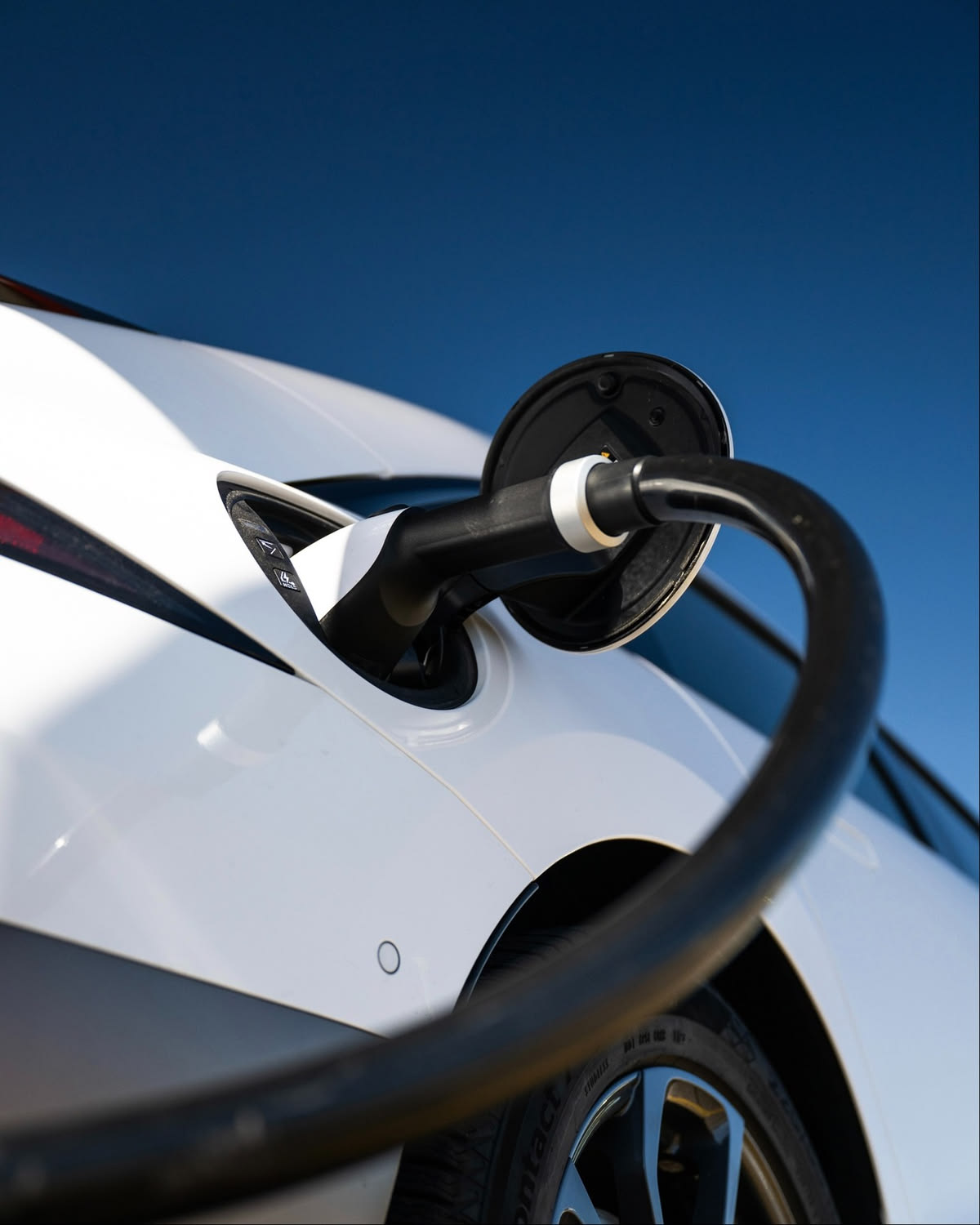 A charging cable connected to the charge port of a white electric car