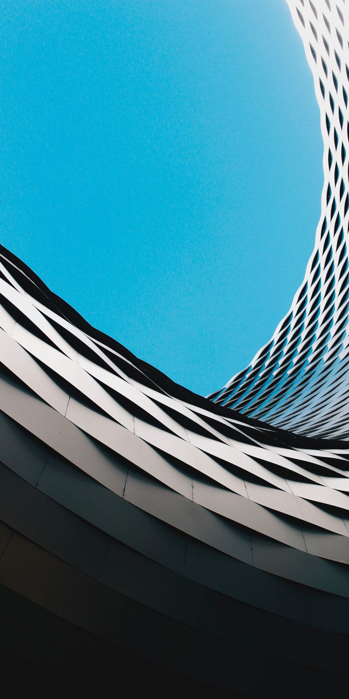 A curved louvred building facade seen from below against a clear sky