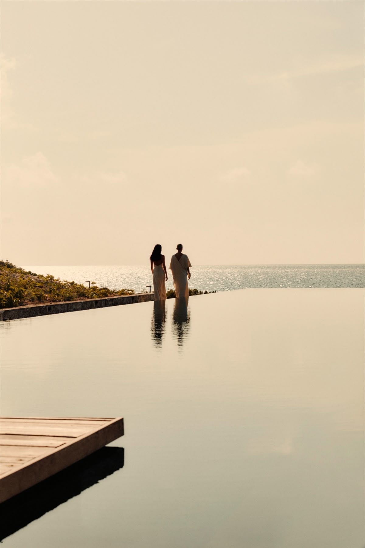 Two people walking beside an infinity pool overlooking the sea at golden hour